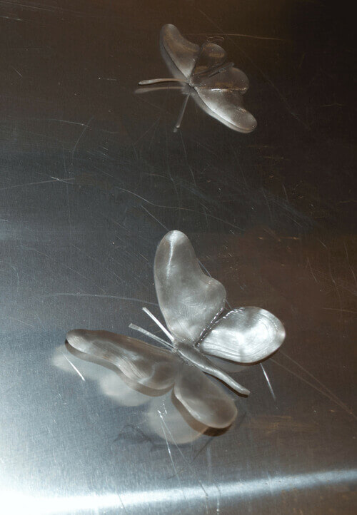 Silver butterflies made of sugar sit atop a steel surface.